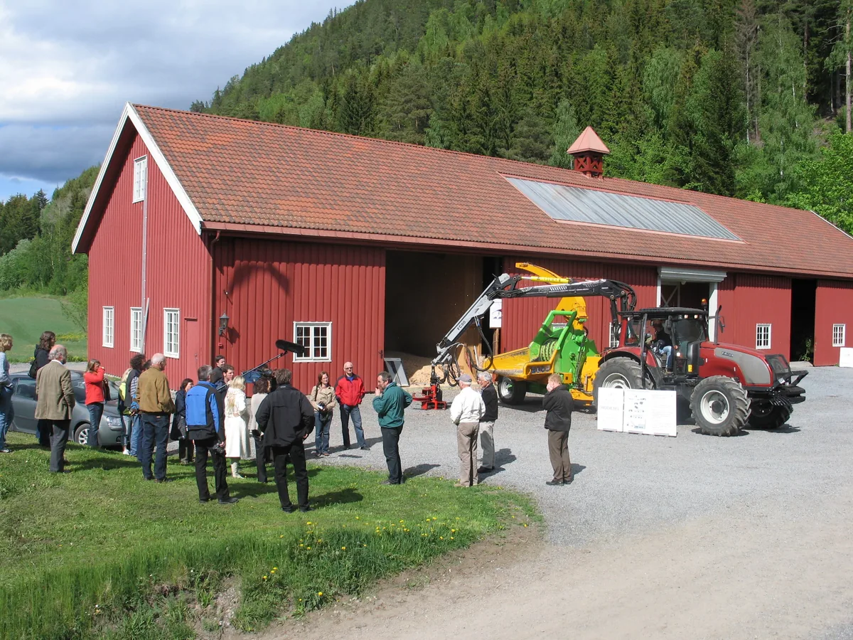 Stor gruppe besøkende foran låven på Eidsalm følger en flishoggerdemonstrasjon.